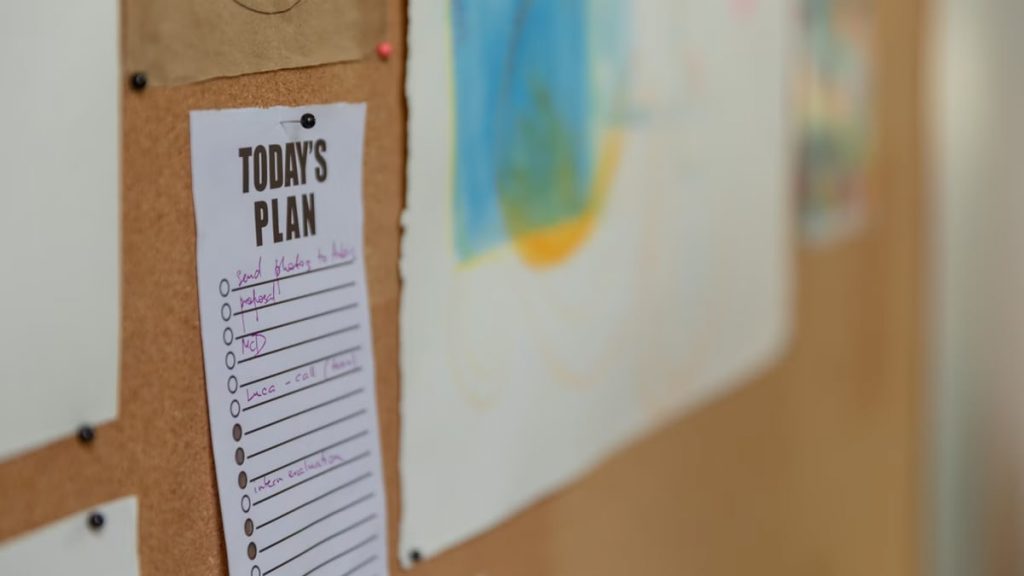 Close-up of a corkboard with a to-do list and colorful artwork in an office setting.